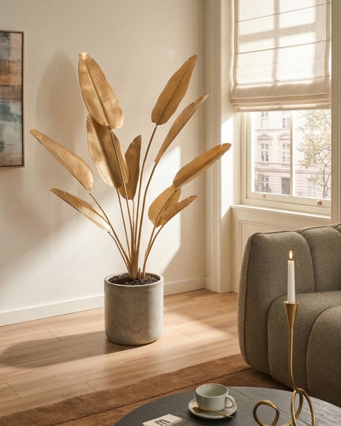 Künstliche Bananenpflanze in Gold im grauen Topf in Betonoptik, modernes helles Wohnzimmer mit Parkettboden und Sofa.