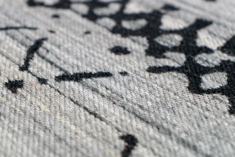 Detailaufnahme eines gewebten Teppichs mit grauem und schwarzem abstraktem Muster und strukturierter Oberfläche.