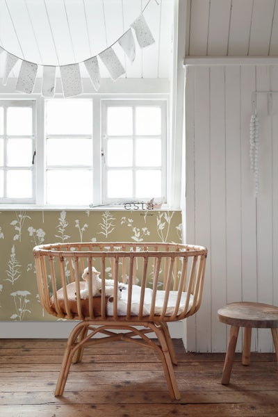 Ein Kinderzimmer mit einem Babybett aus Rattan, einem Hocker und einer Girlande