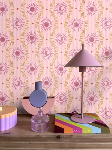 Dekorative Szene mit Mustertapete, Lampe und Deko-Objekten auf einem Tisch