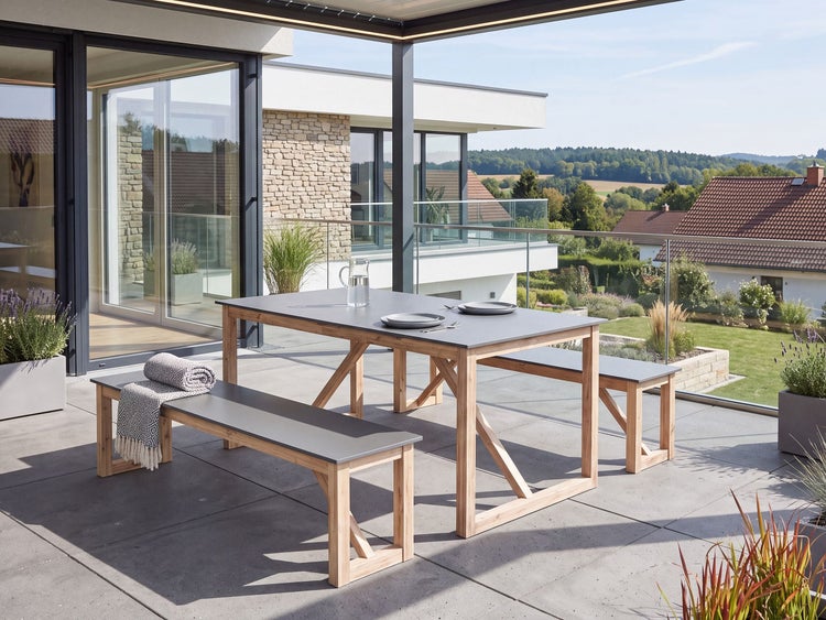 Gartentisch mit zwei Bänken aus Holz und Tischplatten in Steinoptik auf einer sonnigen Terrasse vor einem modernen Wohnhaus.