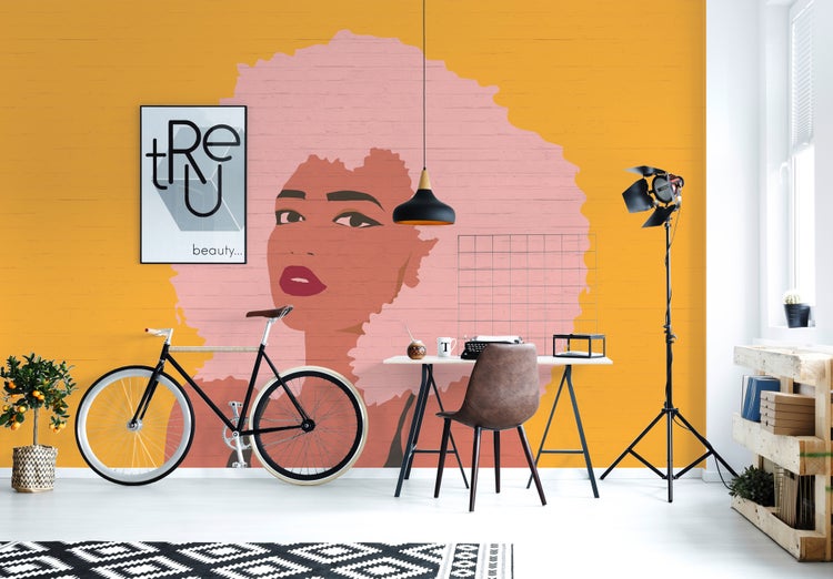 Moderner Arbeitsplatz mit Fototapete eines Frauenporträts auf gelber Ziegeloptik. Inklusive Schreibtisch, Fahrrad und Studioleuchte.