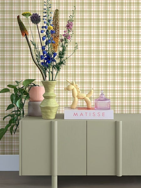 Dekoratives Stillleben mit Blumen, Vase und Zierobjekten auf einem Sideboard vor einer karierten Tapete.