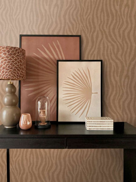 Wohnzimmer dekoriert mit Tapete mit Wellenmuster, Bilderrahmen mit Palmenblattmotiv, Tischlampe, Glasglocke und einer dekorativen Schachtel.
