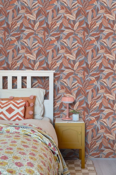 Schlafzimmer mit Vliestapete im Blättermuster, weißem Holzbett mit gemusterten Kissen und gelbem Nachttisch.