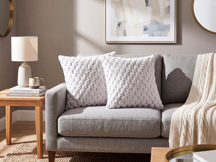 Graues Sofa mit zwei Kissen mit Wabenstruktur und einer beigefarbenen Strickdecke in einem modern eingerichteten Wohnzimmer.
