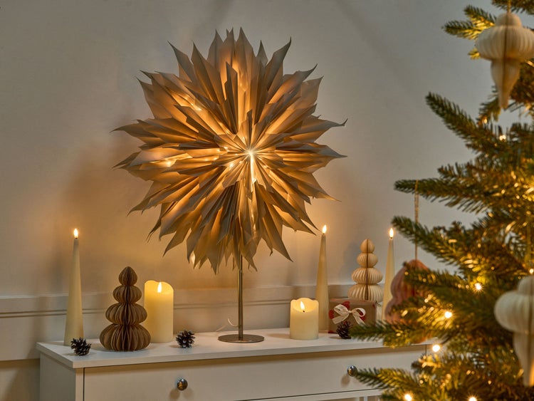 Festliche Szene mit Papiersternleuchte, Kerzen und geschmücktem Weihnachtsbaum auf einer Kommode