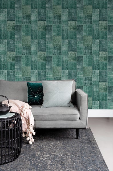 Wohnzimmer mit grauer Couch, Kissen, Beistelltisch, Decke und grüner Patchwork-Tapete