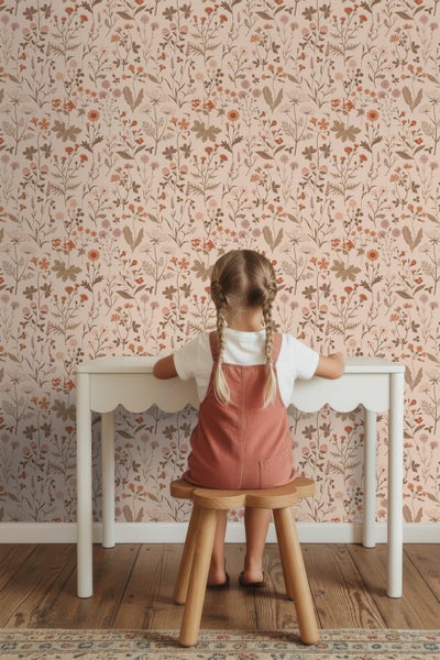 Mädchen sitzt an Kindertisch vor Tapete mit Blumenmuster