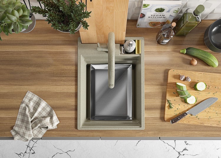 Ansicht von oben auf eine Spüle mit Armatur, Schneidebrett, Gemüse und Küchentüchern auf einer Küchentheke.