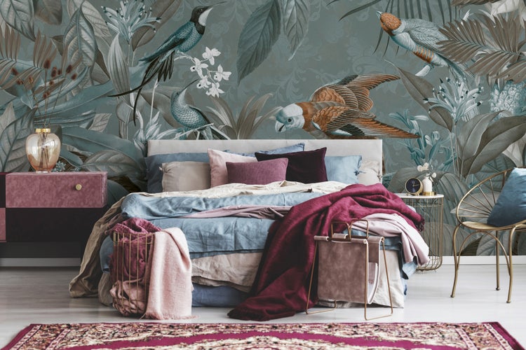 Schlafzimmer mit großformatiger Fototapete mit Tropenvogel- und Blattmotiv hinter einem Bett mit Textilien und dekorativen Elementen.