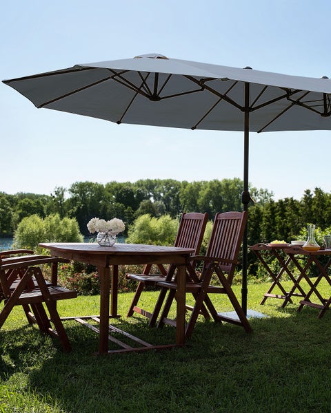Gartenmöbel Set aus Holz bestehend aus Tisch, Klappstühlen und großem lichtgrauem Sonnenschirm auf einer hellen Rasenfläche.