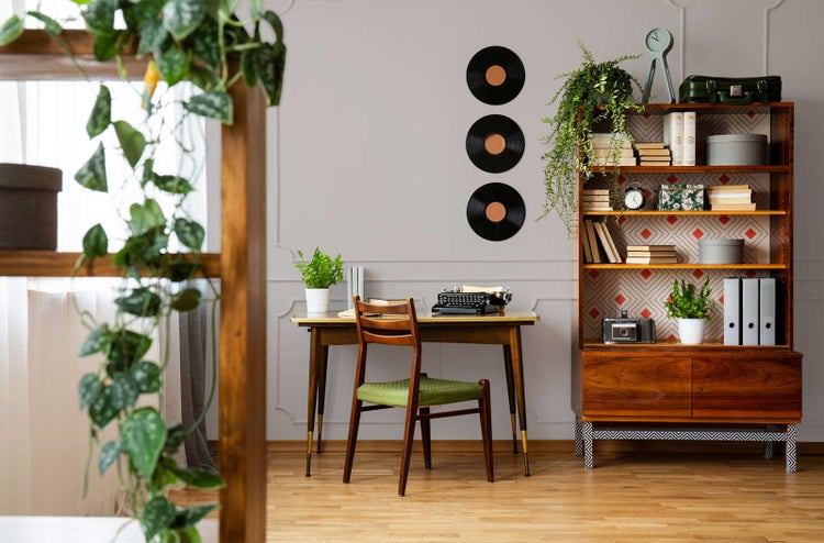 Hell eingerichteter Arbeitsplatz im Vintage-Stil mit Holzschreibtisch, Schreibmaschine und Bücherregal an einer hellgrauen Wand.