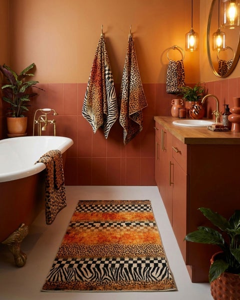 Badezimmer mit freistehender Badewanne, Waschtisch mit Holzplatte, Messing-Armaturen, Handtüchern und Teppich mit Tiermuster sowie Pflanzen.
