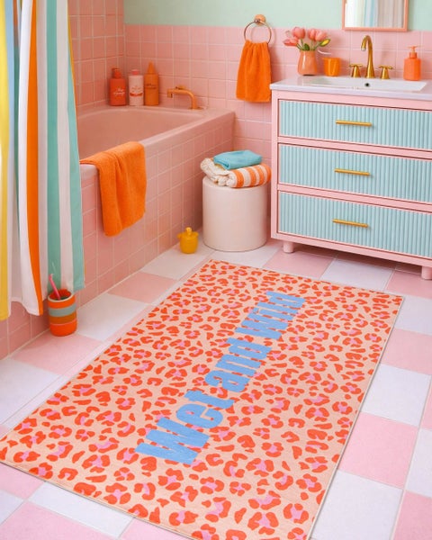 Buntes Badezimmer mit Badewanne, Waschtisch mit geriffelten Schubladen und einem Badteppich im Leopardenmuster mit dem Schriftzug Wet and Wild.