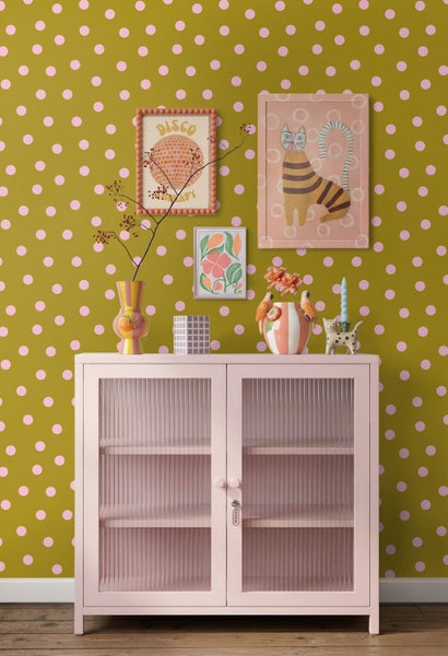 Vliestapete mit Punktemuster hinter einem Sideboard mit Glastüren und Dekorationsobjekten wie Vasen und Bildern.