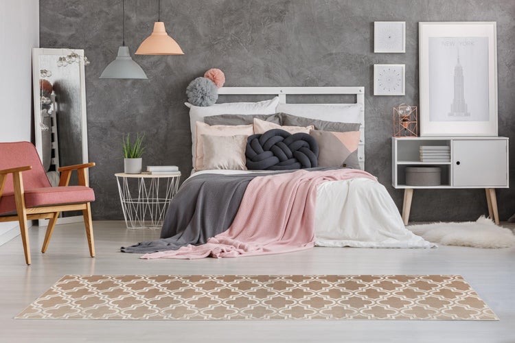Modernes Schlafzimmer mit grauem Strukturputz, weißem Bett, rosa Sessel und gemustertem Teppich in Beige und Weiß.