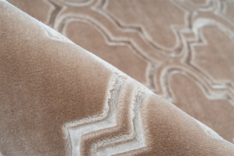 Nahaufnahme eines weichen beigen Teppichs mit geometrischem Muster und dichtem Flor.