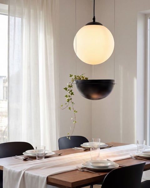 Moderne Esszimmereinrichtung mit Holztisch und Gedecken. Über dem Tisch hängt eine kugelförmige Pendelleuchte mit integrierter Pflanzschale.