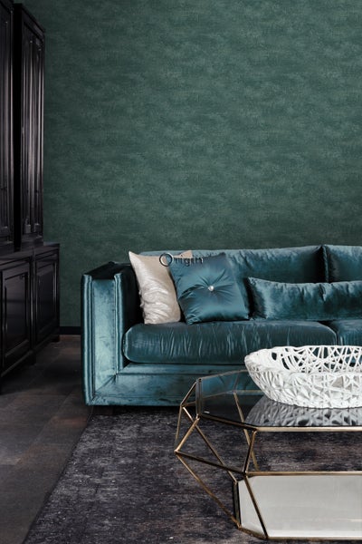 Wohnzimmer mit petrolfarbenem Sofa, Couchtisch und schwarzem Schrank vor einer grünen Wand