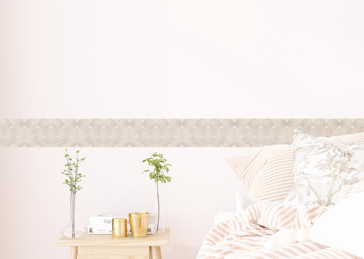 Tapetenbordüre mit gepunktetem Bogenmuster an einer Wand hinter einem Sofa mit Kissen und einer Schale Birnen in einem hellen Wohnraum.