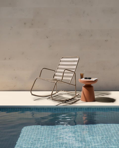 Szene mit einem Schaukelstuhl, Beistelltisch, Buch und Glas neben einem Pool