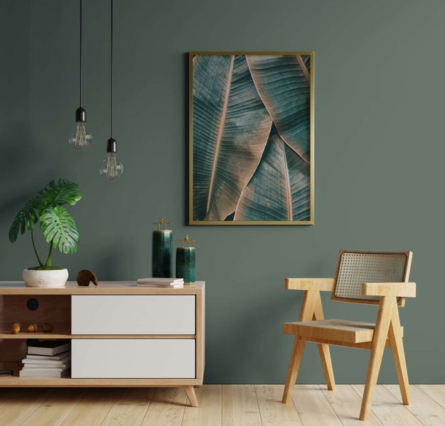 Eingerichteter Wohnraum mit Holzkommode, Holzstuhl mit Geflecht, hängenden Glühbirnen und einem Bild mit Blattmotiven.