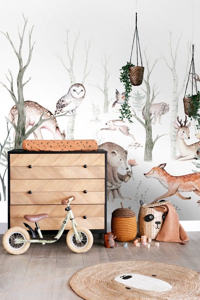 Dekoratives Kinderzimmer mit Kommode, Laufrad, Spielzeugkörben und Waldtapete