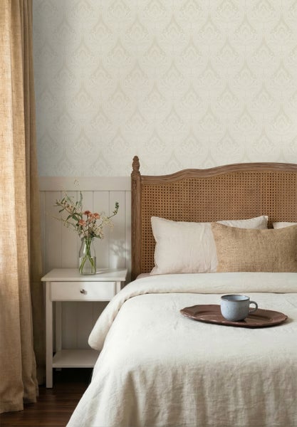 Vliestapete mit hellem Damast-Muster hinter einem Bett mit Holz-Geflecht-Kopfteil und weißem Nachttisch im hellen Schlafzimmer.