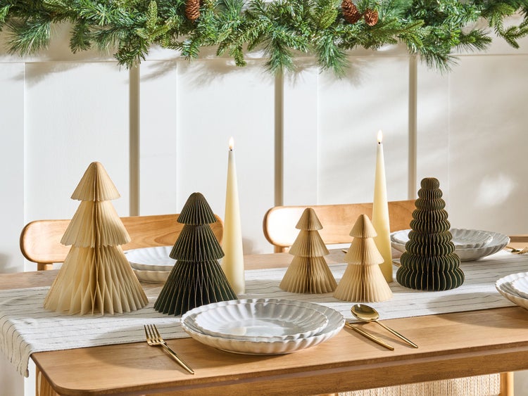 Festlich gedeckter Tisch mit Papier-Weihnachtsbäumen, Kerzen und Geschirr für eine festliche Atmosphäre