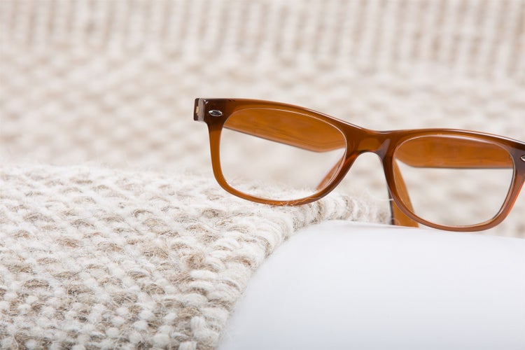 Braune Lesebrille mit Kunststoffgestell auf einem strukturierten Webstoff.