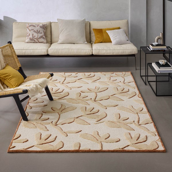 Rechteckiger Teppich mit Blattmuster in Relief-Optik in einem modern eingerichteten Wohnzimmer mit Sofa, Sessel und Beistelltisch.