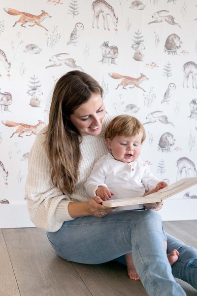 Mutter und Kind betrachten ein Buch vor einer Waldtiertapete
