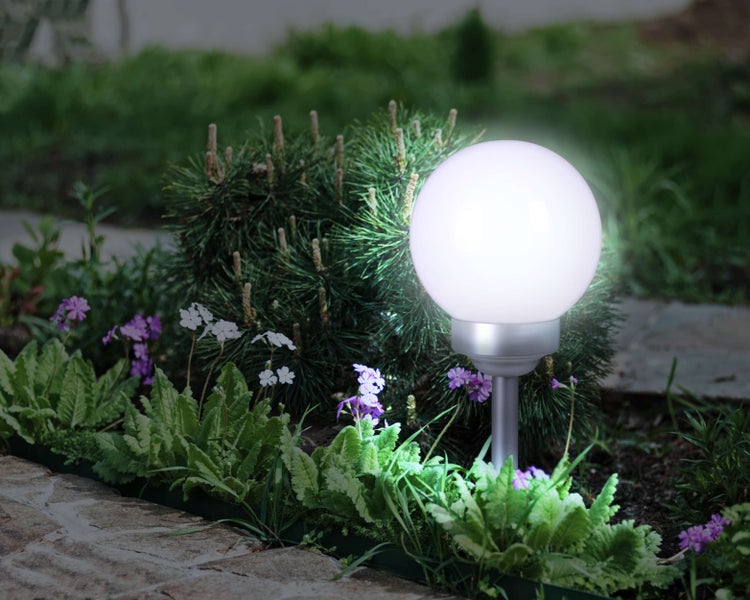 Beleuchtete Kugelleuchte im Garten zwischen Blumen und Büschen