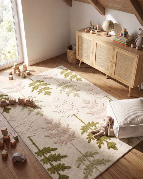 Ein Kinderzimmer mit Teppich mit Blattmuster. Der Raum ist hell, freundlich gestaltet und mit einem Holzschrank und Spielzeug ausgestattet.