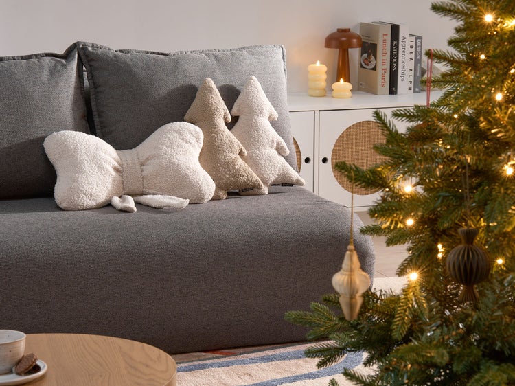 Dekoratives Wohnzimmer mit grauem Sofa, Tannenbaumkissen und Weihnachtsbaum