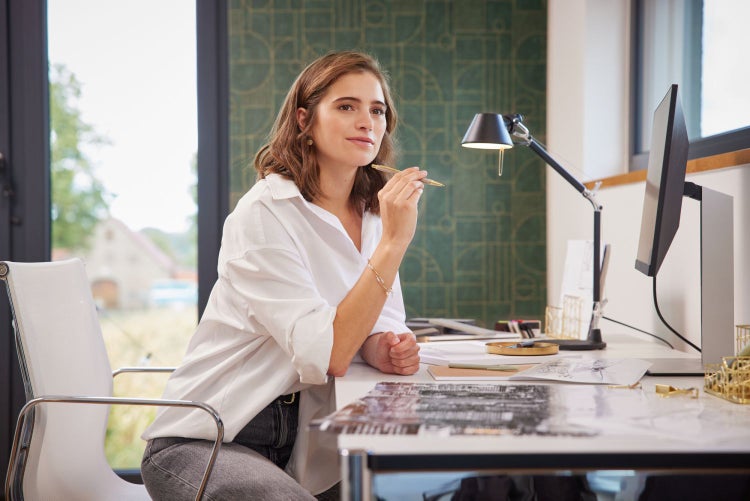 Frau sitzt am Schreibtisch mit Computer und Schreibtischlampe