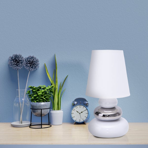 Dekorative Szene mit Tischlampe, Zimmerpflanzen und Uhr auf einem Tisch.