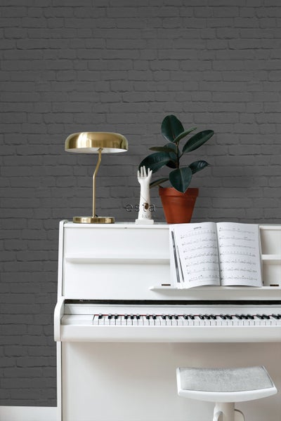 Nahaufnahme eines weißen Klaviers mit Noten, Lampe, Pflanze und Dekor vor einer Wand im Backsteindesign.