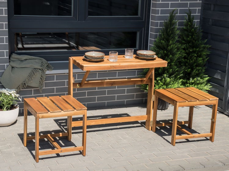 Gartentischgruppe aus Holz mit zwei Hockern, Geschirr und Pflanzen im Freien