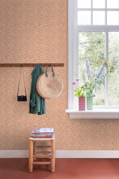 Zimmer mit floral gemusterter Tapete, Holzgarderobe mit Jacke und Tasche, Fenster mit Blumen und Hocker mit Notizbüchern.