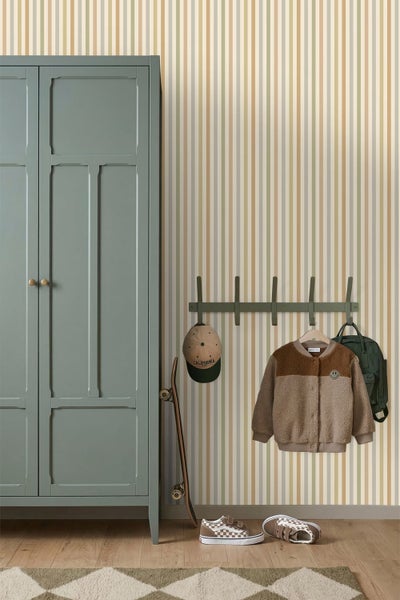 Gestreifte Vliestapete in Erdtönen an einer Wand neben einem grünen Kleiderschrank und einer Garderobe in einem hellen, organisierten Zimmer.