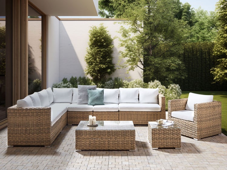 Gartenszene mit Rattansitzgruppe, bestehend aus Ecksofa, Sessel und Tischen.