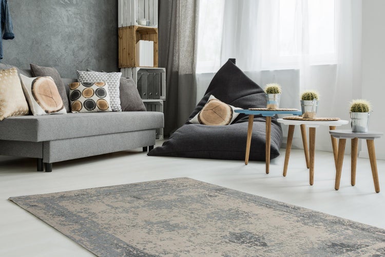 Hell eingerichtetes Wohnzimmer mit grauem Stoffsofa, dunklem Sitzsack, drei runden Beistelltischen und einem gemusterten Teppich in Grau und Beige.