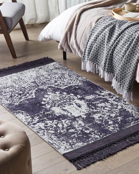 Rechteckiger Teppich mit Vintage-Muster und Fransen auf Holzboden im Schlafzimmer neben einem Bett.