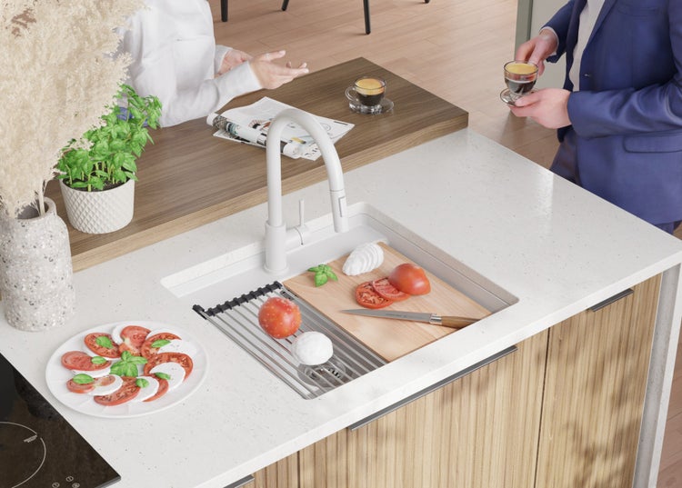 Küchenszene mit Spüle, Armatur, Schneidebrett mit Tomaten und Mozzarella sowie Personen im Hintergrund