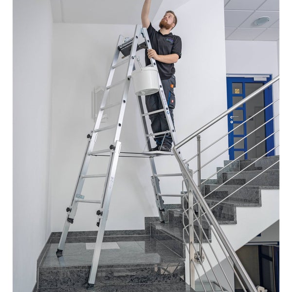 Aluminium-Vielzweckleiter mit Treppenfunktion wird von einem Mann für Malerarbeiten im Treppenhaus genutzt.