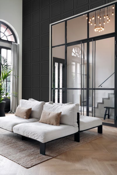 Helles Sofa mit Kissen in einem Wohnzimmer mit dunkler Akzentwand und Glastür.