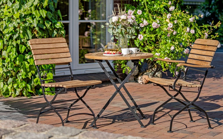 Gartenszene mit Holztisch und zwei Stühlen auf einer Terrasse mit Blumen