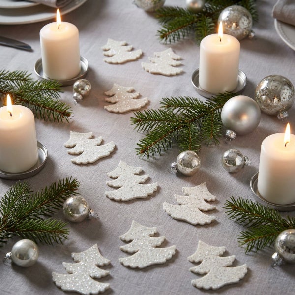 Festlich dekorierter Tisch mit Stumpenkerzen, Tannenbaumschmuck, Tannenzweigen und glitzernden Tannenbaum-Figuren als Streudekoration